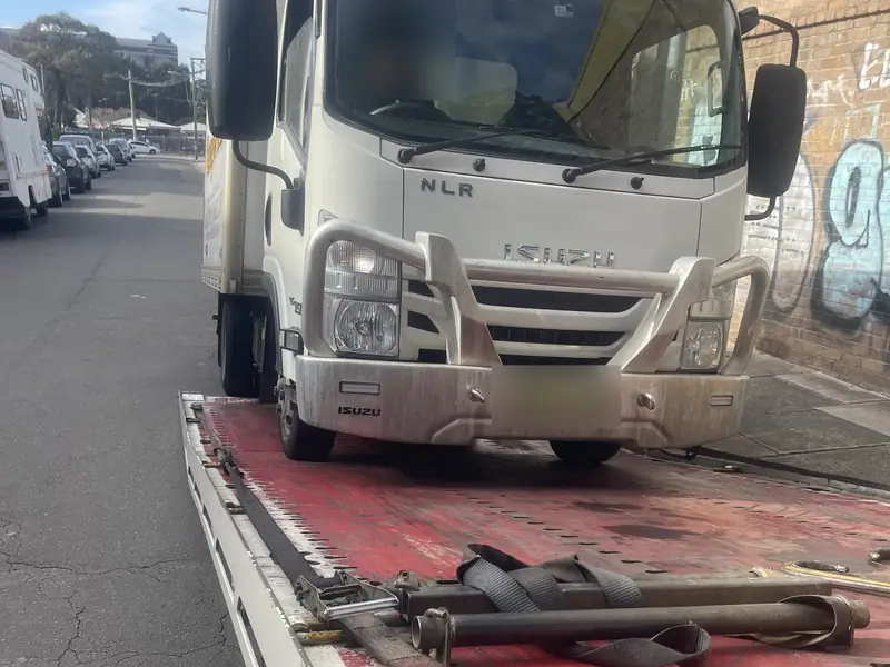 Isuzu light truck being loaded onto a tilt tray tow truck