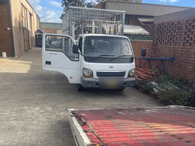 Tilt tray tow truck lowered to pick up a small truck from a laneway