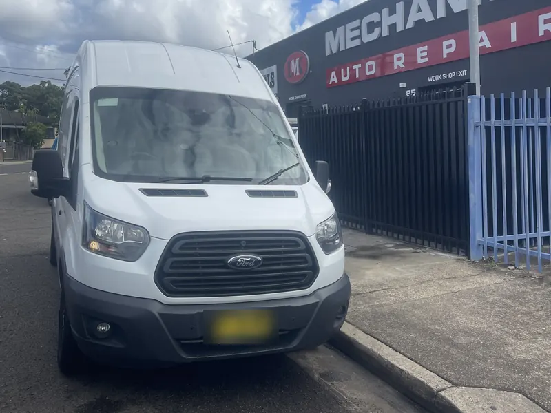 White Ford Transit van parked at an auto repair shop waiting for a tow